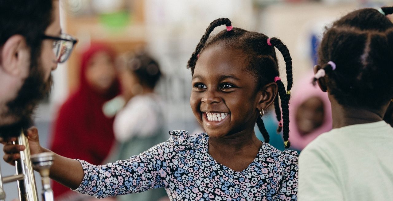 Photo of a child smiling and looking towards musician holding a trombone - in our early years R&D session.
