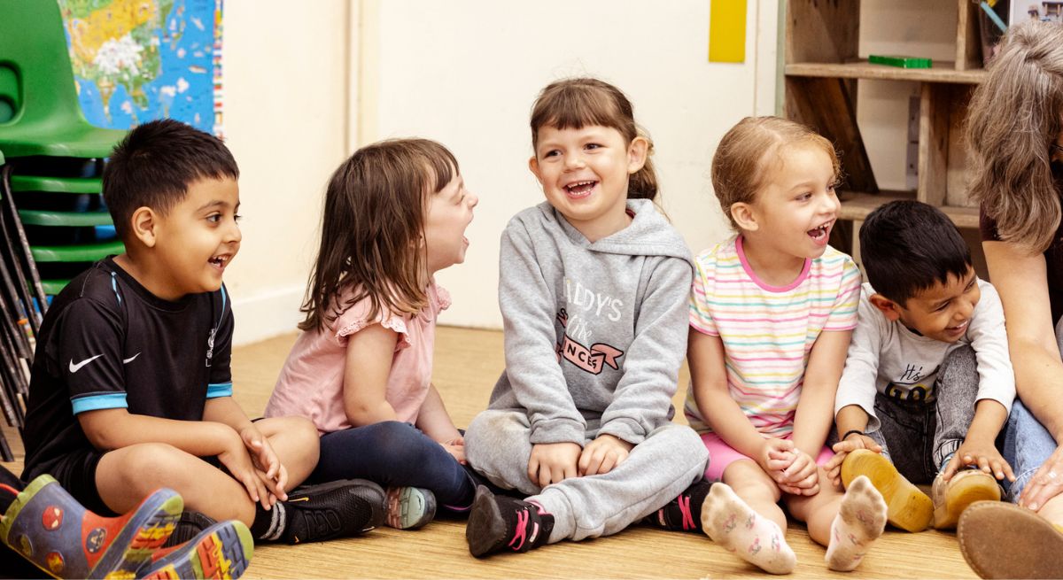Nursery children sitting in a row and laughing during a Light Up Language workshop.