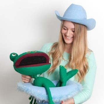 Georgina Densley - a photo of Georgina holding a puppet green frog and wearing a blue cowboy hat.