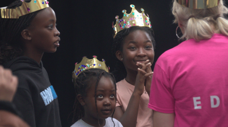 3 young people wearing golden crowns listening to an adult.