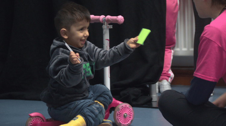 Child holding a post-it note and a pen with a big smile.