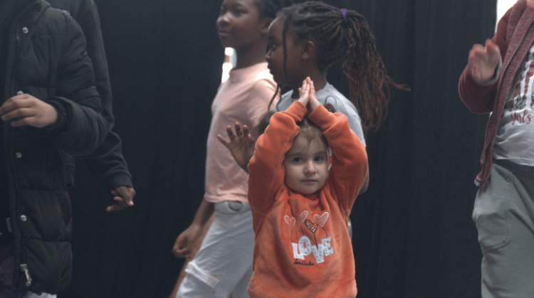 A child with his arms raised above his head with two young people behind him.